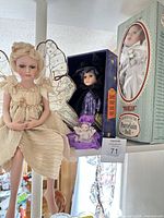 Overview of three boxed/displayed porcelain dolls including Morgan box on right, witch doll in center box, fairy doll seated left, miniature baby doll front