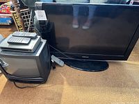 Samsung flat-screen TV on stand, CRT TV with DVD/VCR and remotes stacked