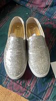 Top view of both silver glitter Michael Kors slip-on sneakers on couch