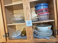 Cabinet shelf showing stacks of plates, bowls, glass bowls, plastic containers