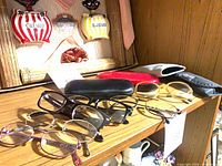 Overall lot showing multiple eyeglasses and three cases on wooden shelf