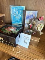 Front view of black lacquered music-jewelry box showing floral lid, label, drawer and surrounding items