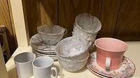Stacked gray marble bowls and saucers, two white mugs, pink mug on floral saucer