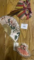 All three fans pinned to wood panel: large silk bird fan, feather fan, small pink satin fan