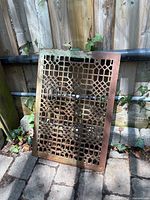 Full view of grate leaning against fence showing overall size and patina