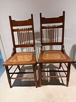 Front view of both oak chairs showing spindle backs and cane seats