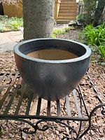 Side view of large black coated terra cotta planter on stand
