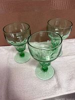 Front view of three matching green Depression glass goblets
