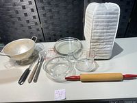 Entire lot laid out showing colander, utensils, measuring cup, bowls, mitt, rolling pin