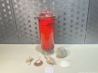 Group shot of red glass apothecary jar with lid and five assorted shell ornaments plus large clam shell