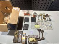 Overview of lot on table with glass knobs, backplates, hinges, hinge stops, chain guard, box of parts