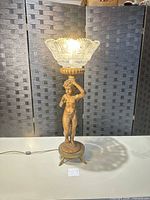 Full view of lit lamp showing figure base, pedestal and glass shade