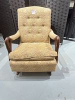 Front view of upholstered rocking armchair showing tufted back, removable cushion, carved wooden arms