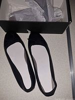 Top view of both black ballet flats next to box