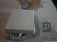 White panel antenna with attached coax and N connector beside mounting plate in plastic with screws