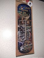 Front view of packaged Rivers Edge tin thermometer with cabin artwork and temperature scale visible