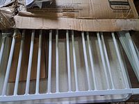 Unassembled white metal gate sections partially out of damaged cardboard box
