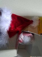 Santa hat next to open box showing white pom-pom in plastic