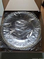 Box opened showing stack of clear plates wrapped in plastic with gold bead edging