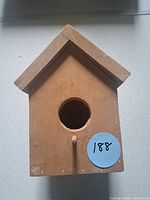 front view of unfinished wood birdhouse showing round entry hole and perch