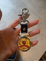 Front view showing gold-tone cover with crest and lobster clasp attachment