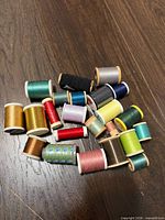 Group of mixed wooden and plastic spools in various colours displayed on dark floor