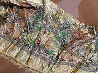 Full view of gold silk brocade tablecloth with children at play scenes and fringe