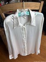 Front view of white shiny blouse on hanger