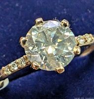 Close-up of ring showing centre diamond, prongs, accent stones, and gold band