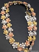 Full view of tri-color gold flower necklace laid flat