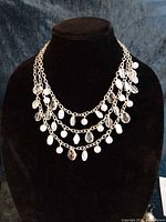 Triple-strand necklace on black bust displaying clear and white beads and faux pearls