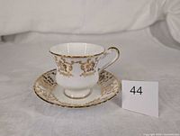 Teacup on saucer with gold decoration, lot tag visible