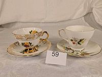 Both teacup and saucer sets side-by-side showing patterns and gold trim