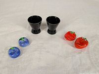 Overall lot showing two black cups, two blue pieces, two red strawberry pieces