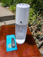 Front view of white SodaStream soda maker with instruction manual