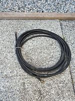 Coiled 50' black porous rubber soaker hose on ground