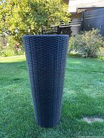 Full view of tall black woven-look planter standing on grass