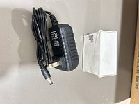 Adapter with coiled cord and barrel connector beside white box