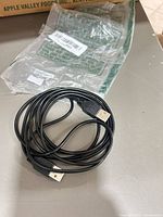 Coiled black USB-A to USB-A cable on surface, packaging in background