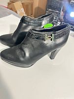 Left side view of both black ankle boots showing smooth faux leather, crocodile-embossed ankle strap, tapered heel