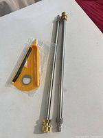 Two stainless steel extension wands with brass/steel quick-connect ends alongside sealed yellow plastic accessory