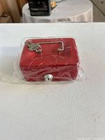 Top view of red metal lock box still in plastic wrap showing handle and keys