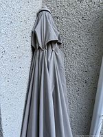 Closed beige/taupe patio umbrella hanging against wall