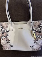 Front view of Calvin Klein white floral tote showing print, logo, handles, visible stains