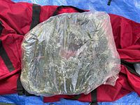 Plastic-wrapped artificial wreath atop red storage bag on tarp