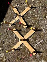 Two wooden cross bases and six wood pegs with painted tops placed on ground
