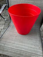 Overall view of red plastic tapered wastebasket on chair