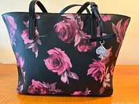 Front view of black vinyl tote with pink floral pattern and charm