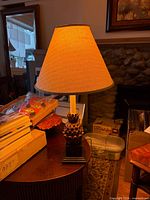 Full view of resin pineapple lamp with lit beige shade on table