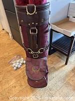 Full view of Wilson Country Club burgundy golf bag with side pocket logo, leather strap, and visible golf balls